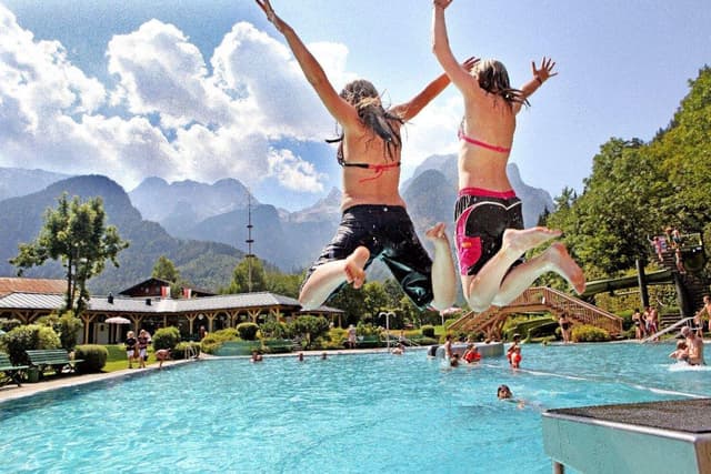 Due ragazze si tuffano allegramente in una piscina. Sullo sfondo si vedono montagne e un bel paesaggio.