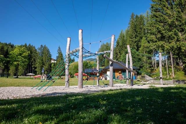 Un parco giochi con una struttura da arrampicata e uno scivolo in un contesto verde. Sullo sfondo si vedono alberi e un paesaggio adatto al picnic.