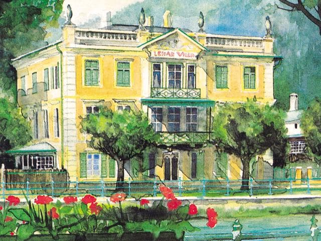 Elegantní vila se žlutou fasádou a zelenými okenicemi. Před budovou kvetou červené květiny a stromy dávají stín.