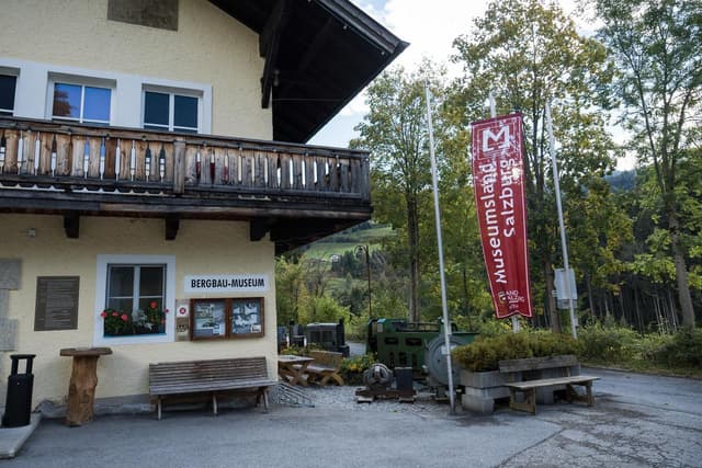 Budynek z balkonem i szyldem muzeum. Przy wejściu stoi duży czerwony baner Bergbau-Museum Salzburg.