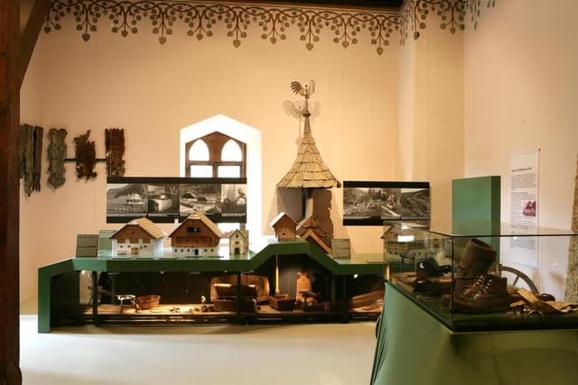 Sala wystawowa z modelami domów i historycznymi przedmiotami. W tle widać zdjęcia i informacje.