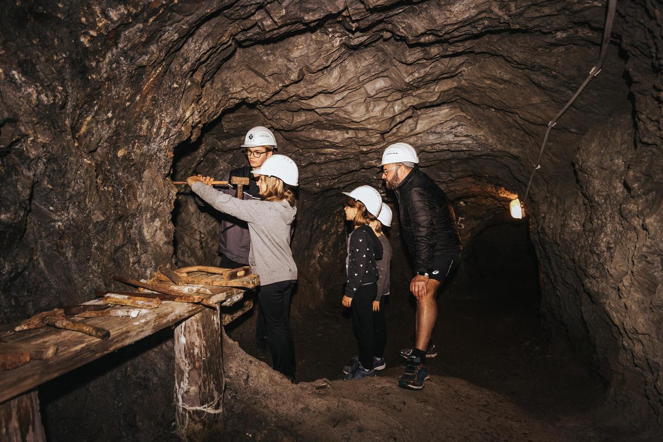 Grupa ludzi w profesjonalnych kaskach zwiedza podziemny tunel. Badają ściany i interesują się historią tego miejsca.