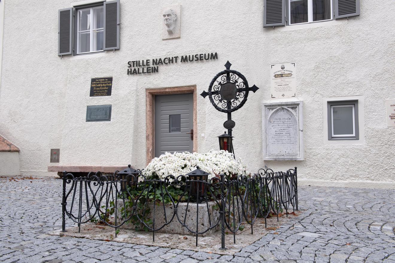 Bílá budova s cedulí „Stille Nacht Museum Hallein“. Před vchodem je záhon s křížem.